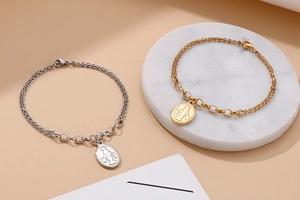 Detail of silver and gold layered coin bracelets with religious pendants on marble