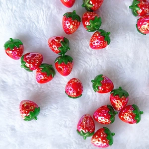Close-up of red acrylic strawberry beads with green leaves on white plush surface