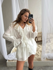Détail d'un ensemble chemise blanche à volants avec col en V et cordons aux manches