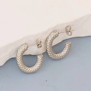 Close-up of silver geometric C-hoop earrings with detailed scale-like woven texture