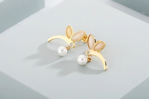 Close-up of gold dragonfly earrings with pink cat-eye stones and white imitation pearls