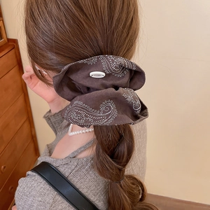 Brown paisley pattern scrunchie hair tie shown on a ponytail in a warm home setting