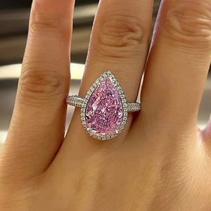 Macro shot of a pear-shaped pink gemstone ring with halo diamond setting on a hand