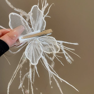 Gros plan d'une pince à cheveux papillon en plumes blanches avec perles et clip métallique
