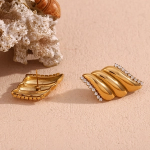 Dettaglio di orecchini ad ala placcati oro 18K con zirconi su sfondo di sabbia materica