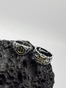 Detail of vintage Poseidon trident and iron cross rings on black volcanic stone