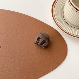 Close-up of a small matte brown resin hair claw clip on a textured leather surface