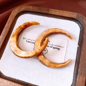 Macro detail of amber resin C-shape hoop earrings with retro tortoiseshell texture on wood