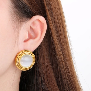 Macro shot of gold textured earrings featuring white cat-eye stones on female model