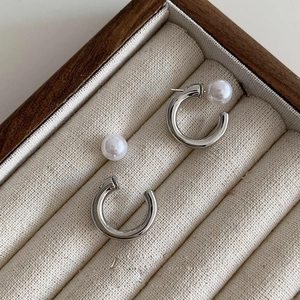 Detail view of silver C-shaped pearl earrings on a soft cream jewelry display tray