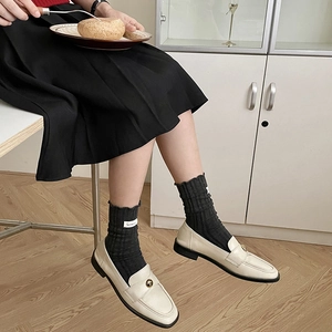 Women's black slouch socks paired with beige loafers and pleated skirt in natural light