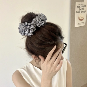 Close-up of a grey satin scrunchie worn on a high bun with elegant pleated fabric detail