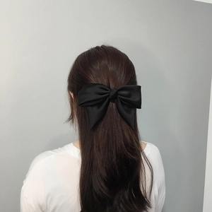 Close-up of a large black satin bow hair clip worn by a model in a half-up hairstyle