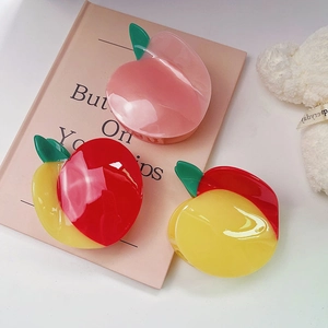 Detailed view of a glossy peach-shaped hair claw clip on a soft pink decorative background