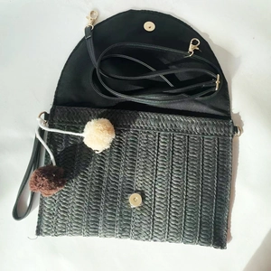 Detail view of black straw envelope bag with decorative pom-poms and interior magnetic snap
