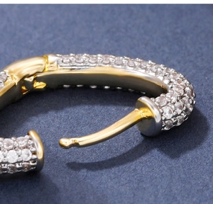 Macro detail of gold pave setting hoop earring with zircon stones on dark background