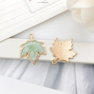 Close-up of green enamel maple leaf charms with gold borders and textured metal back