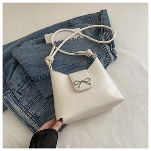 Detail of white PU leather crossbody bag with silver bow accent on denim jacket