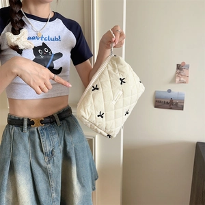 Quilted cream cosmetic bag with black bow embroidery held by a model in a natural setting
