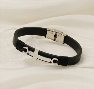 Gros plan d'un bracelet en cuir noir avec croix en acier inoxydable sur fond satiné plissé