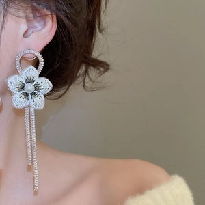 Détail de boucles d'oreilles fleur brodée avec perles et pompons diamantés