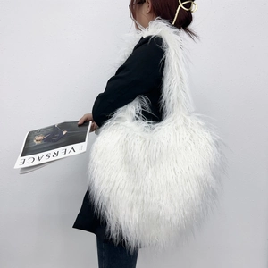 White heart-shaped faux fur shoulder bag worn by model against a minimalist wall