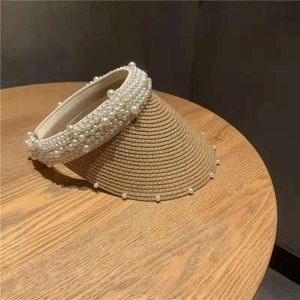 Detailed close-up of straw sun visor hat with faux pearl embellishments on a wooden table