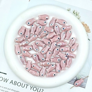 Macro view of pink ceramic fish beads in a white plate for DIY jewelry making