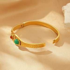 Golden irregular geometric bangle with green and red cat eye stones on silk fabric