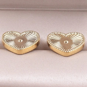 Macro shot of gold heart stud earrings with radial texture and beaded edges in a jewelry box