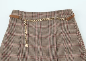 Detail of brown houndstooth trousers featuring a luxury gold chain belt and leather buckle