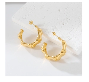 Detailed view of C-shaped golden earrings with natural bamboo texture on stone pedestal