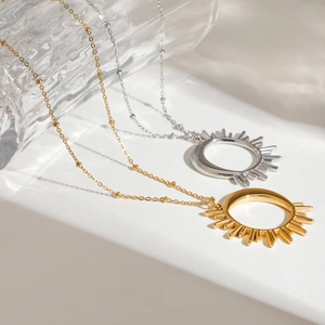 Detailed view of sun-shaped gold and silver stainless steel necklaces on a white surface