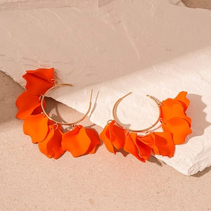 Detail of gold hoop earrings featuring orange acrylic petals on textured stone background