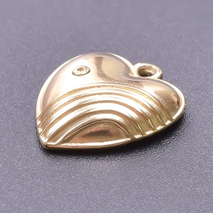 Macro detail of a 18k gold plated heart pendant with engraved lines on textured background