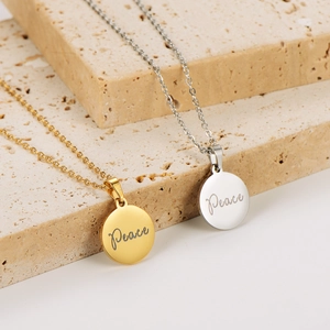 Engraved 18k gold and silver peace pendant necklaces displayed on stone blocks