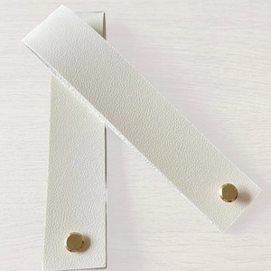Two white PU leather luggage tags with gold snap buttons on light wood background