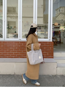 Detail of grey fuzzy fleece tote bag with EVER label carried by a model in camel coat