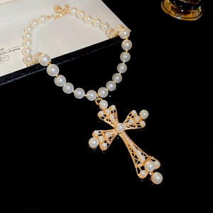 Macro detail of a golden hollow cross pendant necklace with pearls on a black reflective surface