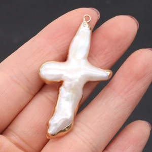Pendentif croix en perle de culture baroque avec bord doré tenu à la main