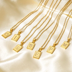 Golden stainless steel rectangle letter necklaces with zircons on beige silk fabric