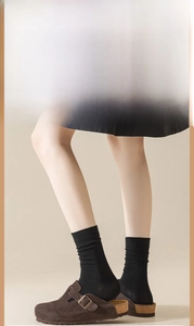 Close-up of brown suede mules with metal buckles worn over black knitted mid-calf socks