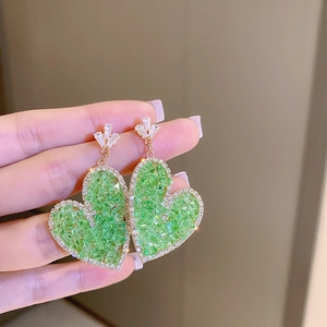 Detailed close-up of green heart crystal earrings with sparkling gold metal backing