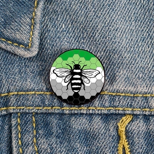 Detail of Aromantic pride flag enamel bee brooch pinned on a blue denim jacket pocket