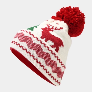 Close-up of knit Christmas hat with red reindeer patterns and fluffy pom-pom detail