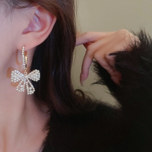 Primo piano di orecchini a fiocco dorati con perle bianche e diamanti indossati da modella