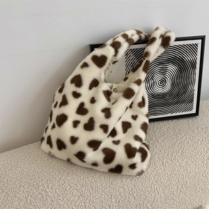 Close-up of white plush tote bag with brown heart patterns and metallic snap closure