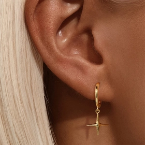 Macro shot of a gold four-pointed star charm on a circular hoop earring worn on an ear