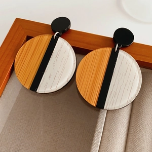Détail de boucles d'oreilles rondes avec grain de bois brun et design en résine noire