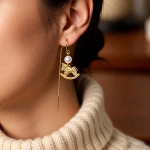Elegant gold rocking horse pearl long earrings worn by a model on a white sweater